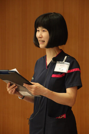 【画像】開会挨拶を務めた看護部長の加藤看護研究発表会も１５年目を迎えました。先ほど看護部総会で、NHKの朝ドラの場面、一ノ瀬りんの父の言葉「正しいことは難しいのう」でありませんが、自己研鑽や看護研究の大切さは分かっていても、実践することは容易ではありません。先月、厚労省で「２０４０年に向けた看護職員の養成・確保の在り方に関する検討会」が始まり、看護職に求められる資質が議論されました。１８歳人口の減少や看護学校の定員割れが続く中、看護師という仕事の魅力向上と継続教育の義務化が課題となっています。医療・看護の専門職として生涯研鑽を続け、量から質への転換を図りながら、やりがいと誇りをもって活躍できる看護の未来に向けて、本日の発表会を盛り上げていきましょう。